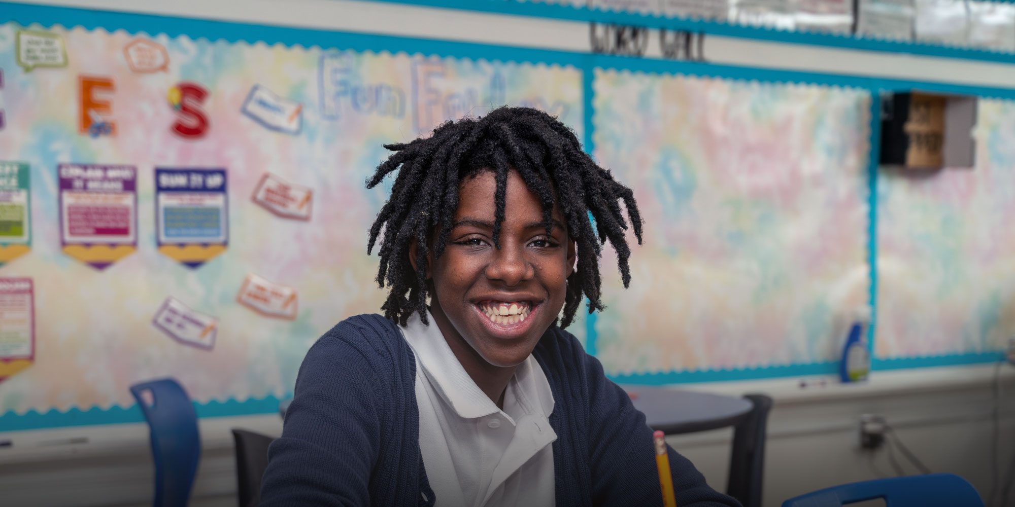 Smiling student sitting at a desk in a Broadway Academy classroom.