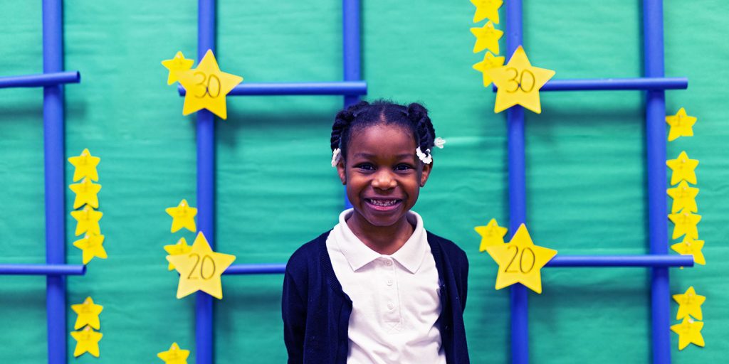 Smiling student in front of hallway achievement board.